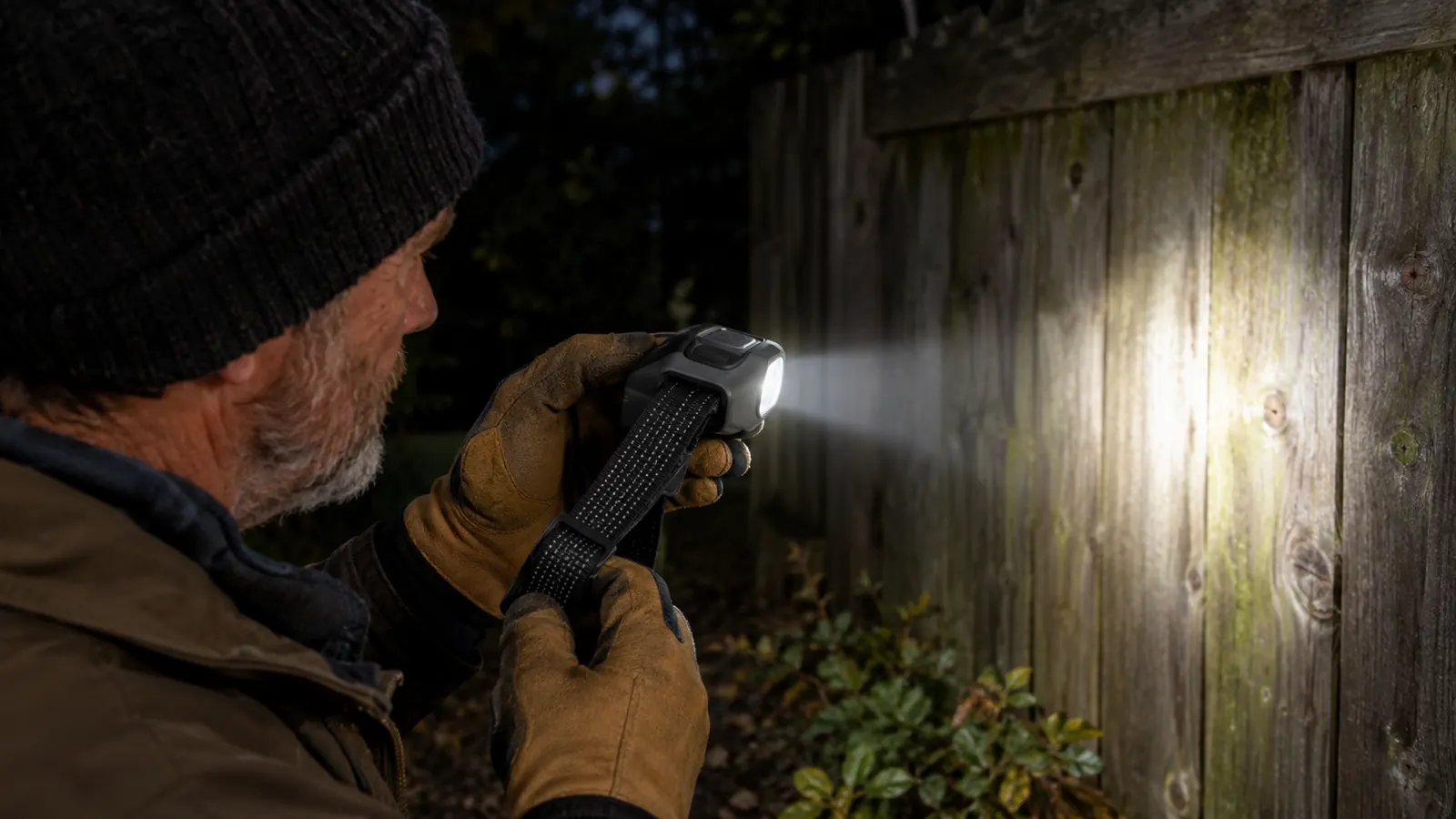 Close-up of a headlamp in hand being switched on against a dark backdrop